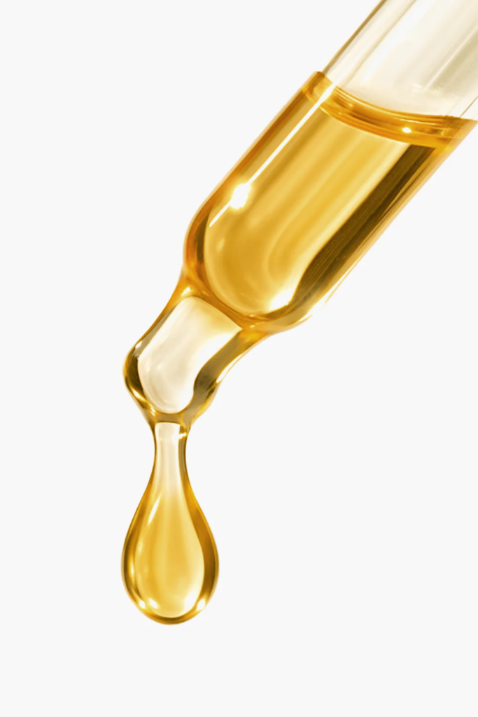 A drop of golden cold-pressed argan oil falling from a glass pipette